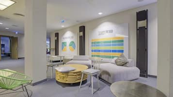 A modern lounge area with seating, a wall-mounted information display, and a visible exit sign.
