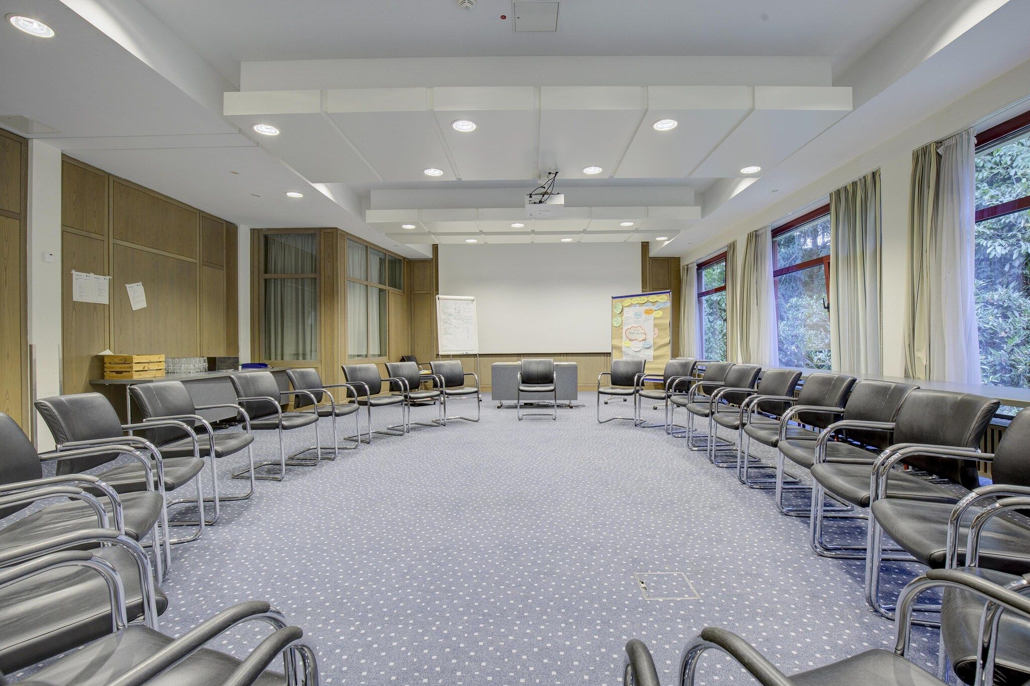 A conference room with a long table, chairs, a projector screen, and a presentation board.