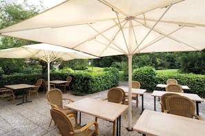 Een terras buiten met tafels en stoelen, beschaduwd door grote parasols.