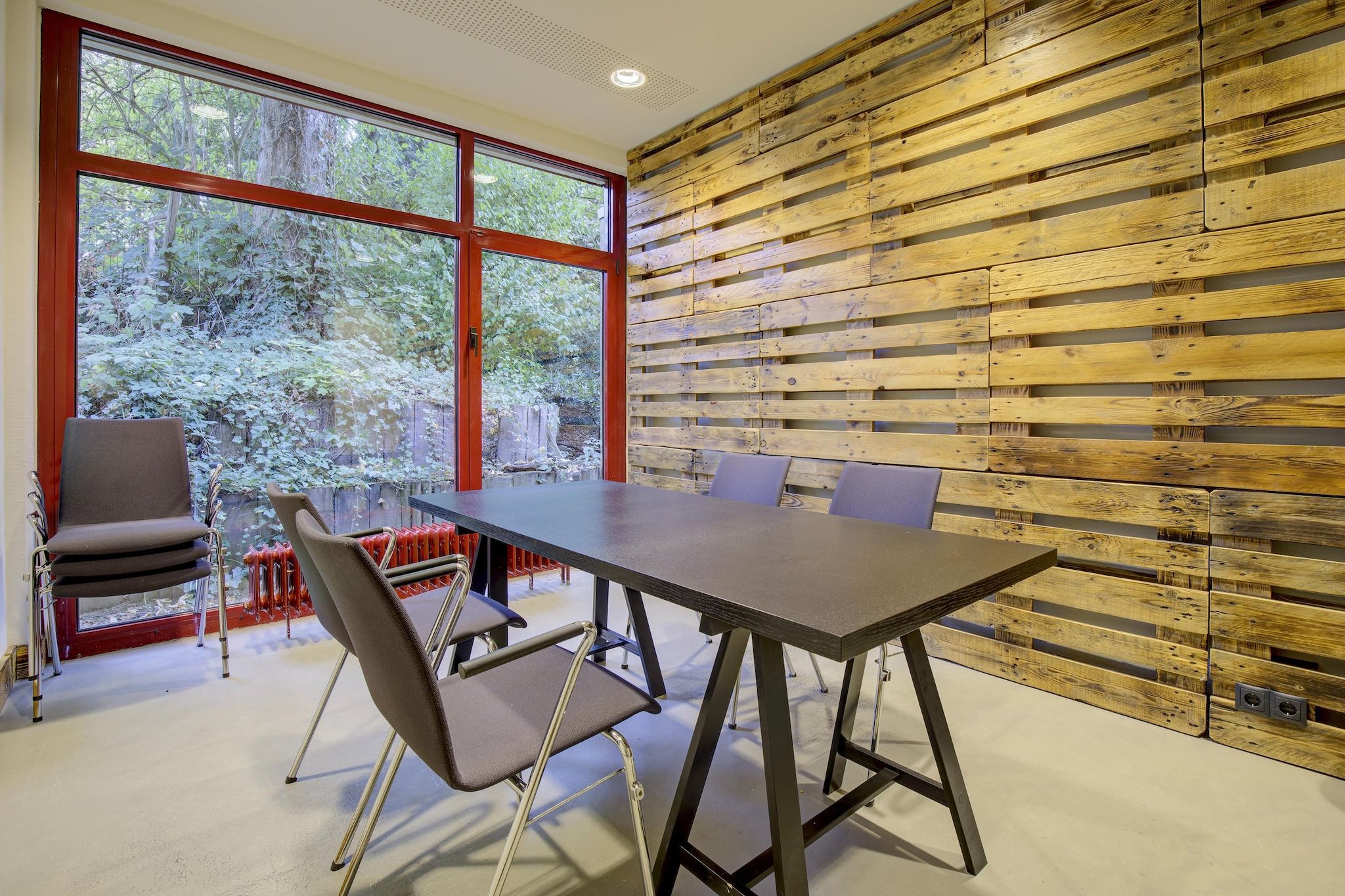 A modern interior with a large table and chairs, wooden panel walls, and large windows.