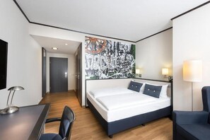 Una habitació d'hotel amb un llit, escriptori, cadira i un ampli quadre abstracte a la paret.