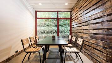 A conference room with a long table and four chairs, a window with blinds, and a wooden wall panel.