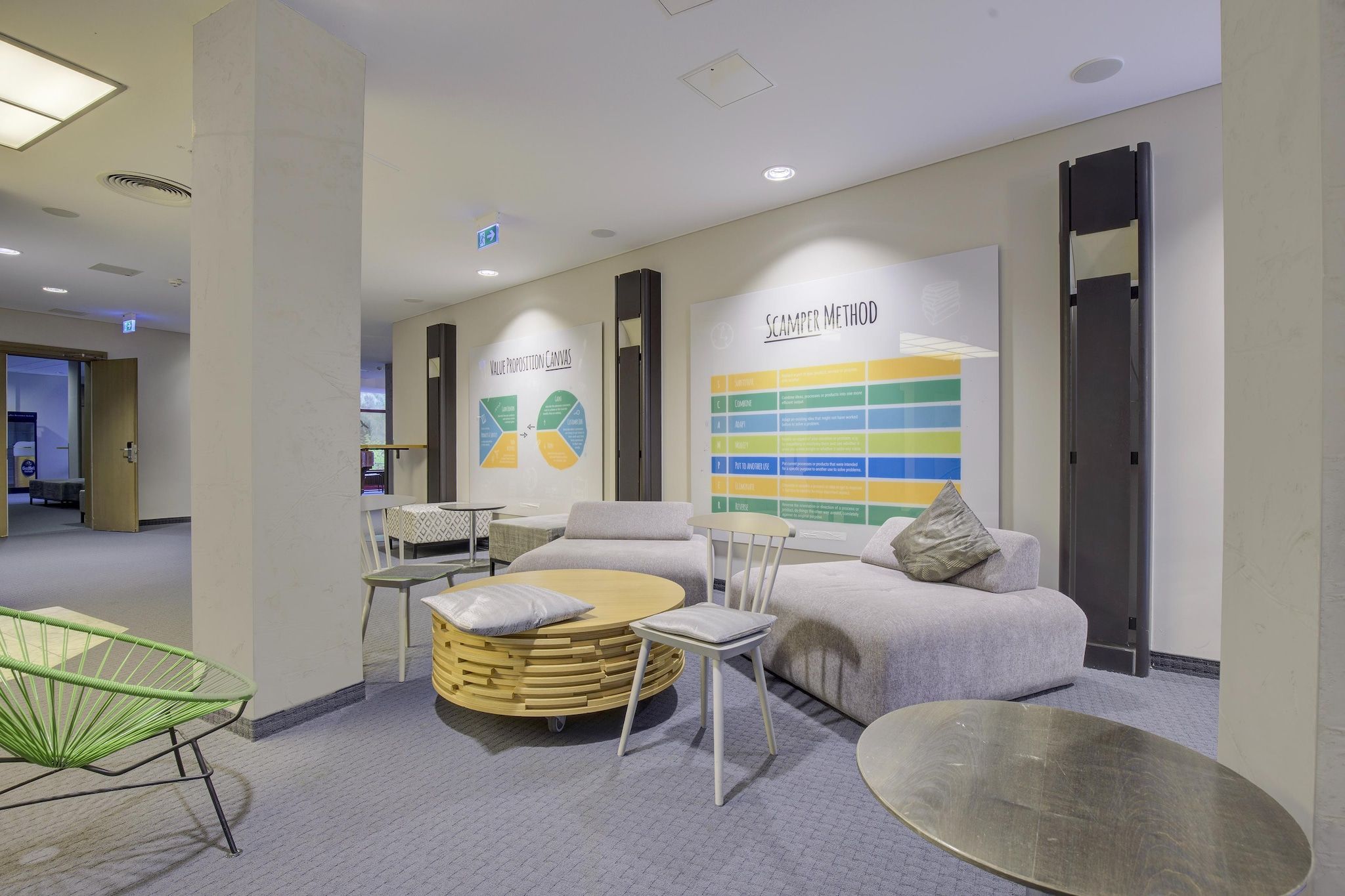 A modern lounge area with seating, a wall-mounted information display, and a visible exit sign.