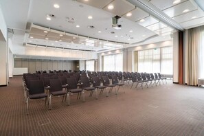 A conference room with rows of chairs, a carpeted floor, and large windows.