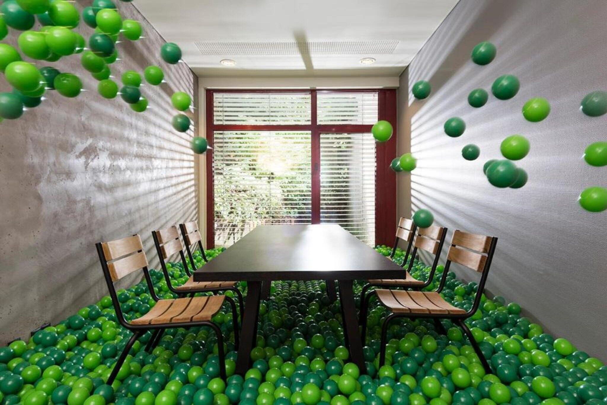 A dining area with a table surrounded by chairs, set in a room with a concrete floor and walls, and a window with blinds.