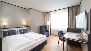 Una camera d'albergo con un letto, una scrivania, una sedia, un televisore e tende.