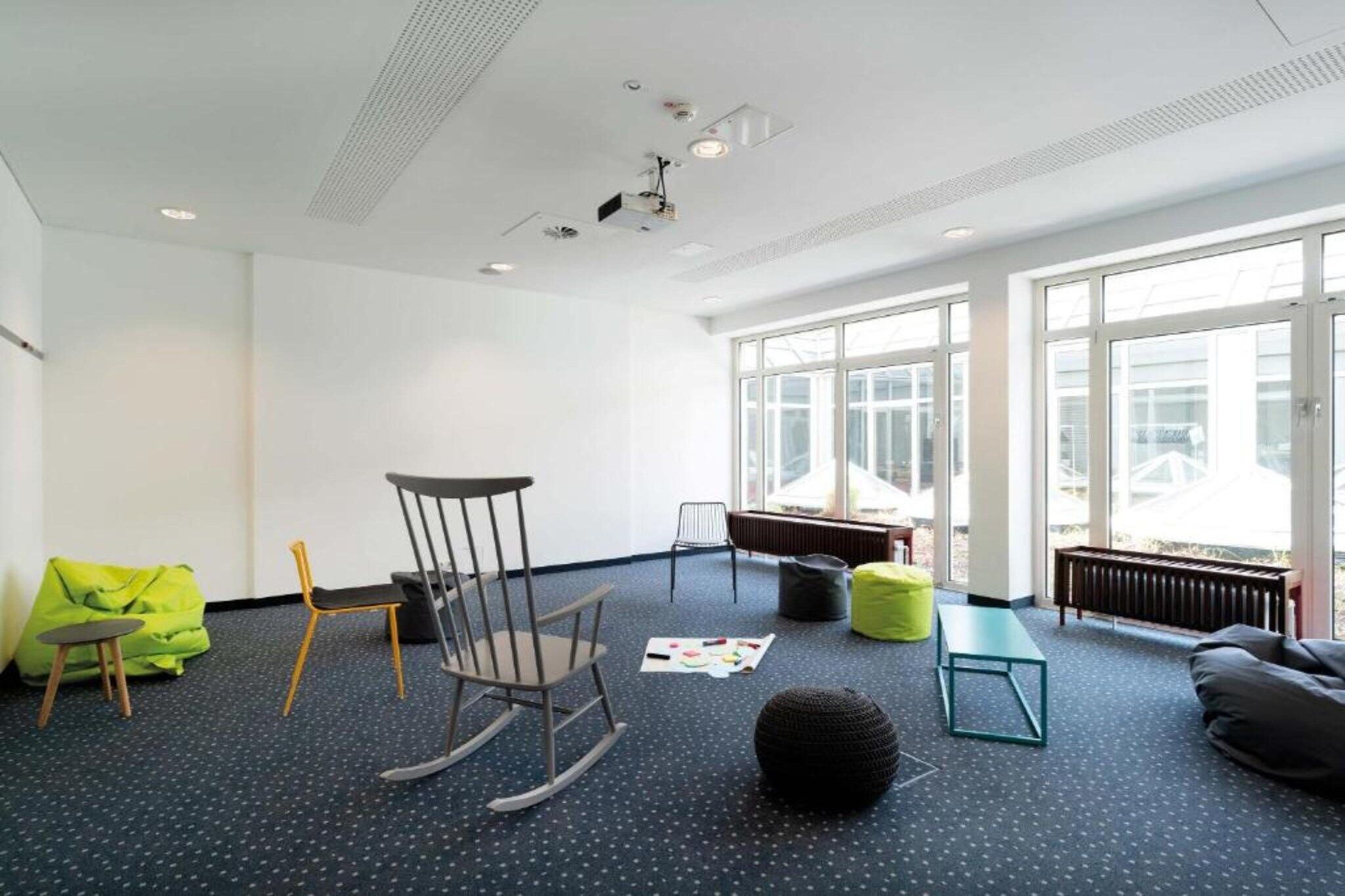 A spacious room with a large window, a rocking chair, a bean bag, a small table, and a radiator.