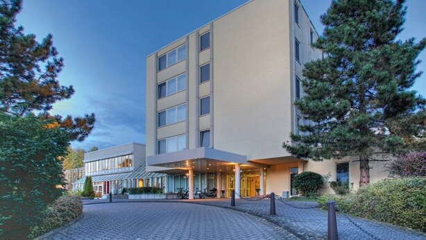 Un hotel moderno con un ingresso centrale, una zona esterna coperta e un parcheggio.