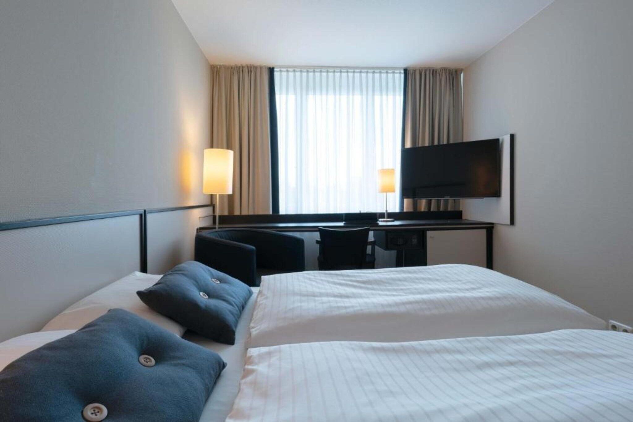 A hotel room with a bed, a desk, a chair, a television, and curtains.