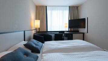 A hotel room with a bed, a desk, a chair, a television, and curtains.
