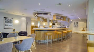 Eine Bar mit Hockern, einer Theke voller Flaschen und gerahmten Bildern an der Wand.