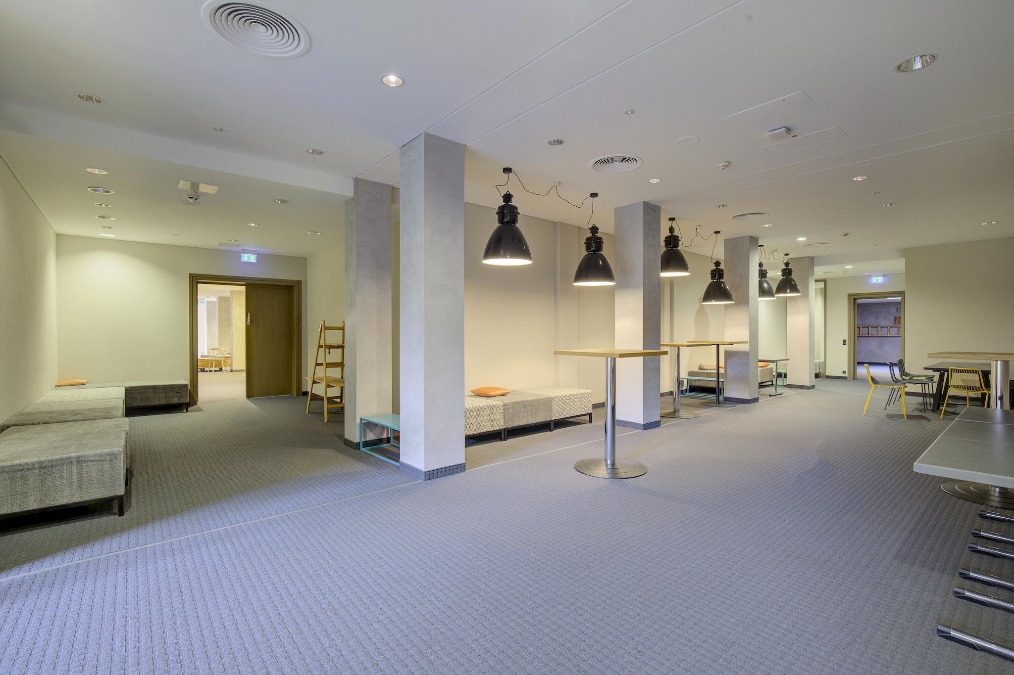 A hotel room with a bed, a desk, and a chair. There are multiple pendant lights and a ceiling vent.