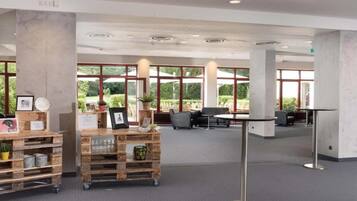 Un espacio interior amplio con ventanas grandes, un carrito de madera con varios artículos y una zona de estar con mesas y sillas.