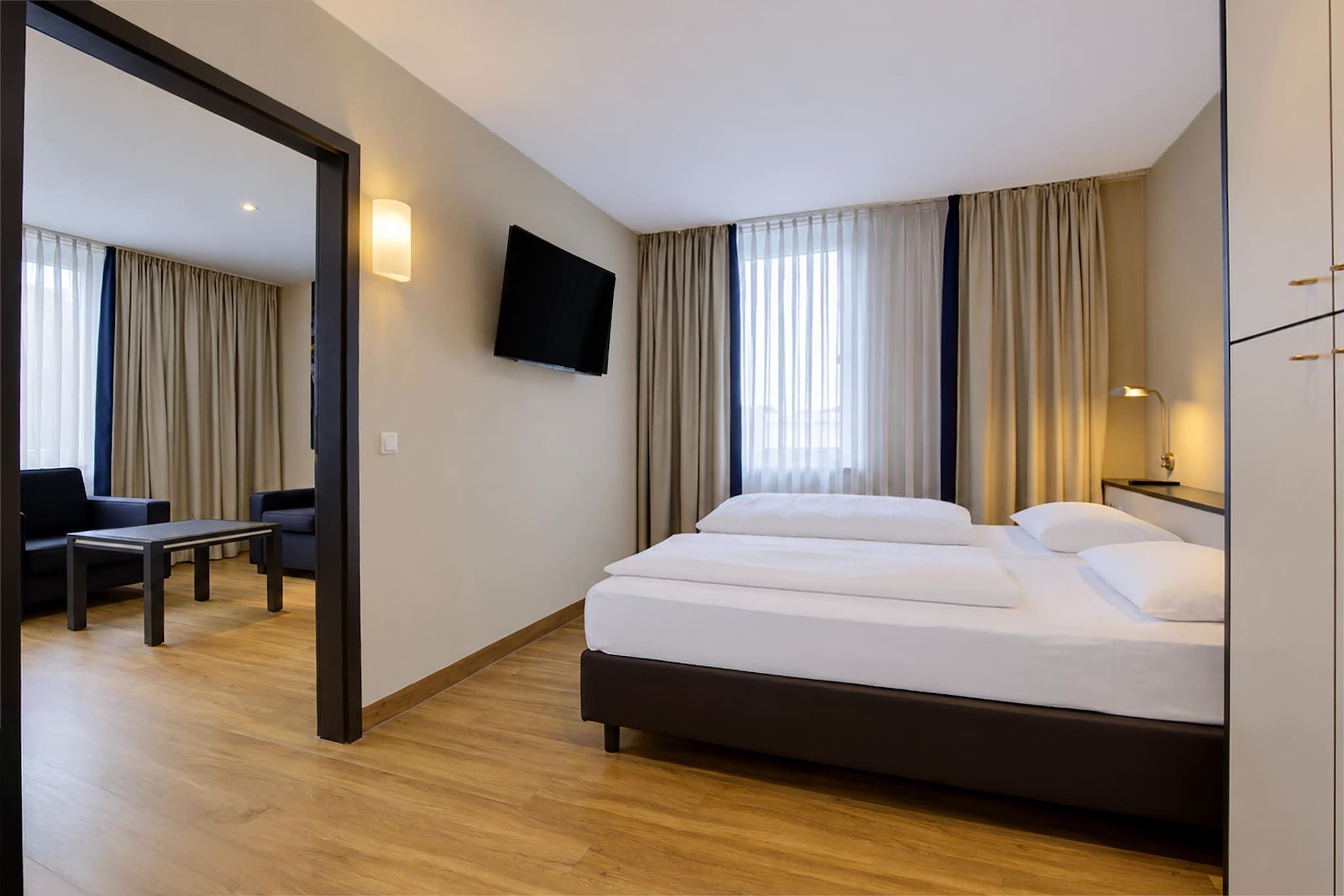 Une chambre d’hôtel avec un lit, un bureau, une chaise, une télévision et des rideaux.
