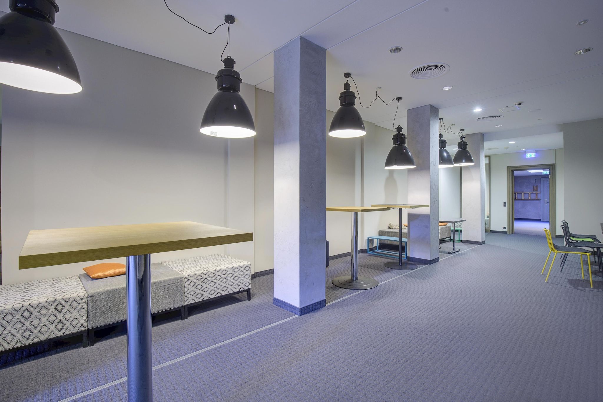 Un intérieur moderne avec un long couloir, des espaces de détente et des luminaires suspendus.