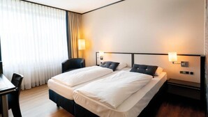 Una camera d'albergo con due letti, una scrivania e una sedia.