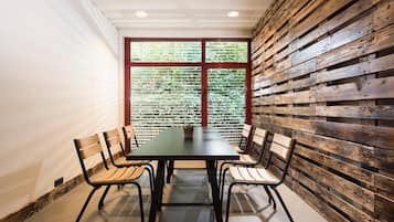 A conference room with a long table and four chairs, a window with blinds, and a wooden wall panel.