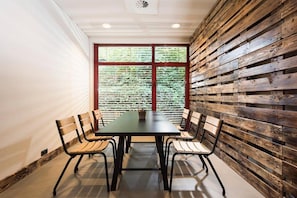 A conference room with a long table and four chairs, a window with blinds, and a wooden wall panel.