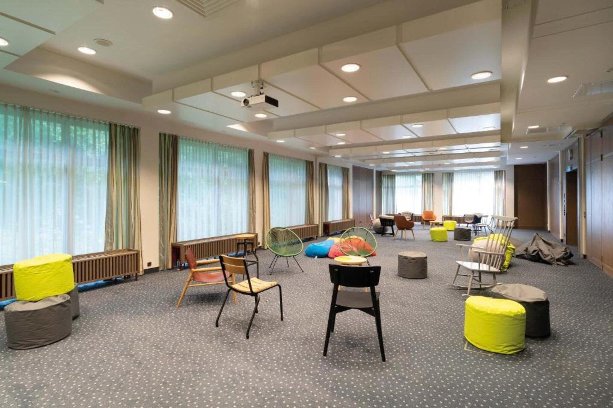 Une pièce spacieuse offrant de nombreuses options d’assises, notamment des chaises et des fauteuils poire, de grandes fenêtres avec des rideaux et un plafond doté d’un éclairage encastré.