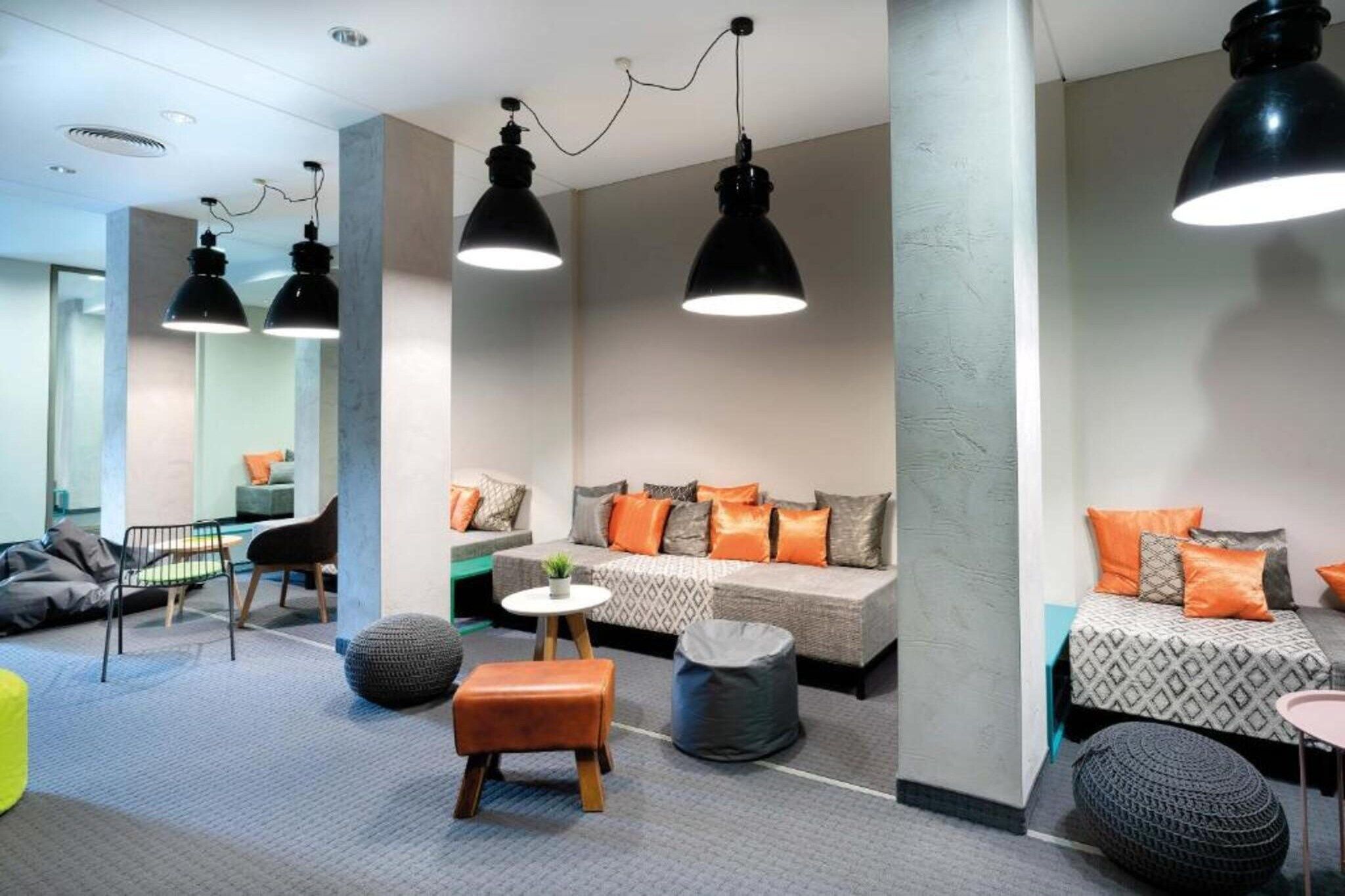 Un espacio lounge moderno con sofás, otomanas e iluminación colgante.