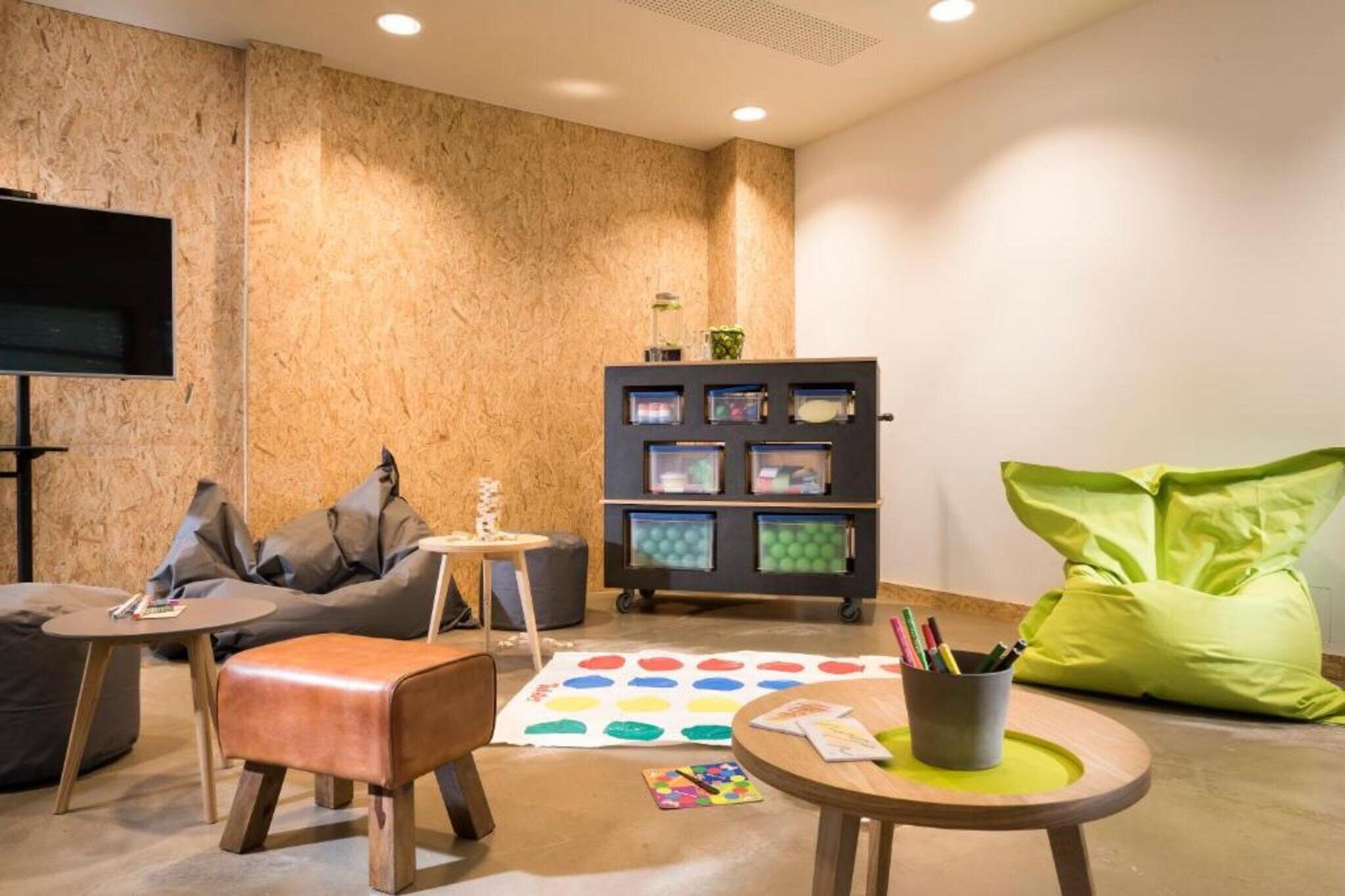 A modern living room with a sofa, a bean bag, a coffee table, a bookshelf, and a flat-screen TV mounted on the wall.