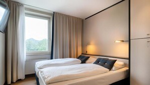 Une chambre d’hôtel avec deux lits, une fenêtre avec des rideaux, un radiateur et une lampe fixée au mur.