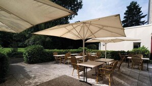 Una terrazza esterna con tavoli e sedie, grandi ombrelloni e un'area giardino.