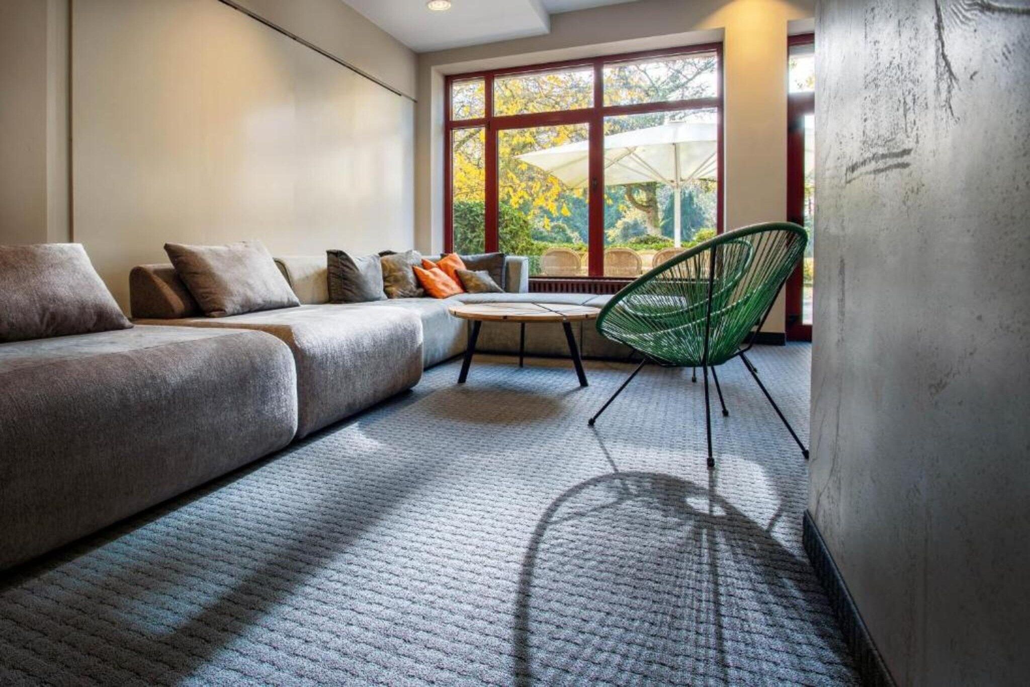 A modern living room with a sectional sofa, a green chair, a small table, and a large window with a view of trees.