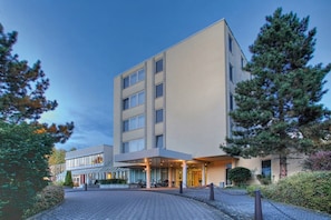 A modern hotel with a central entrance, a covered outdoor area, and a parking lot.