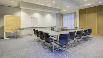 Een vergaderzaal met een grote tafel, stoelen, een whiteboard en een beamer.