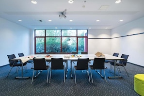 A conference room with a long table, chairs, a projector, and a view of trees through large windows.