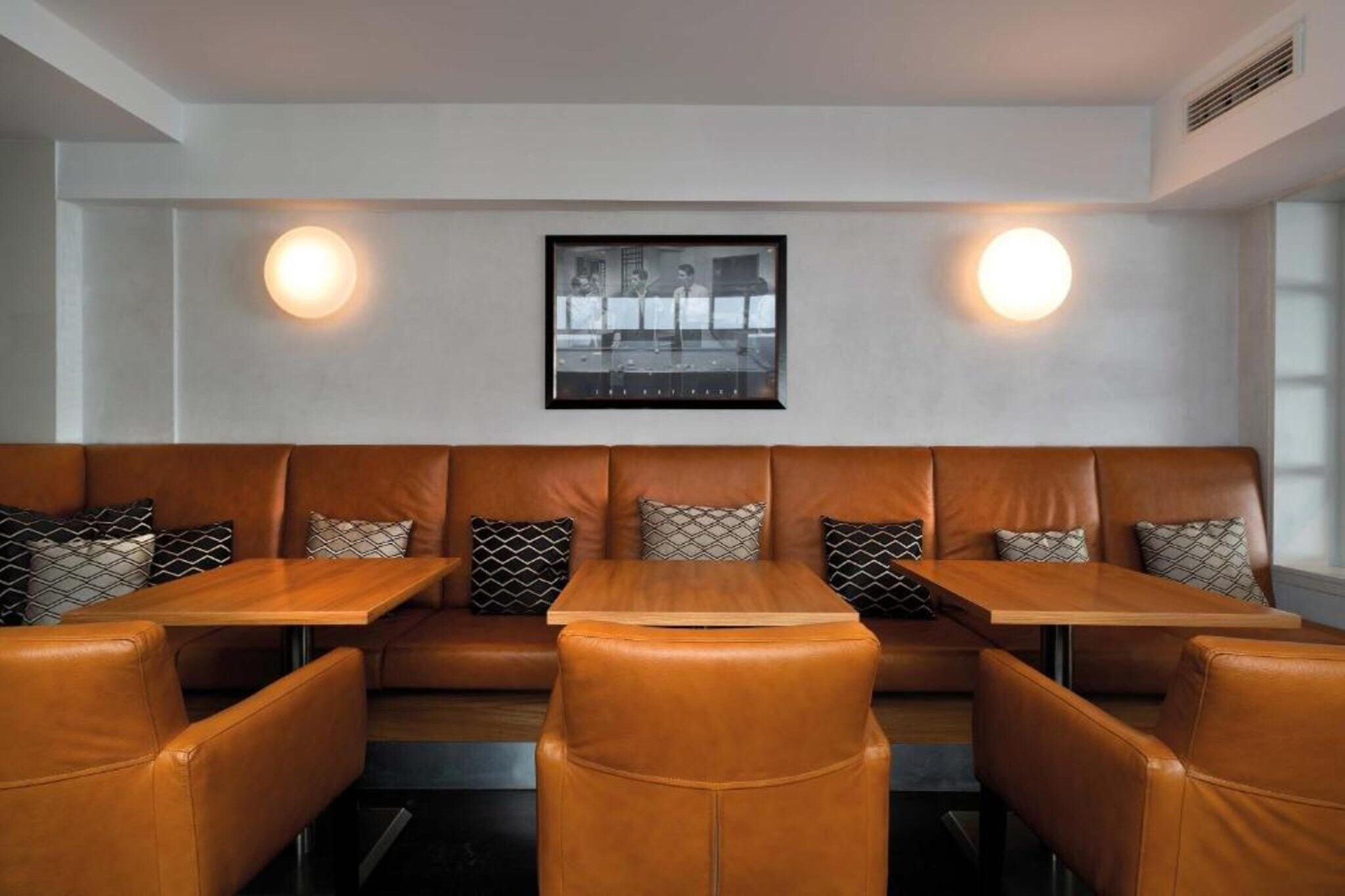 A restaurant with leather booths and wooden tables, featuring wall-mounted lighting and a framed photograph above the seating.
