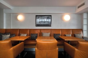 A restaurant with leather booths and wooden tables, featuring wall-mounted lighting and a framed photograph above the seating.