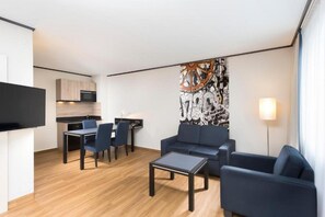 A modern living room with a sofa, coffee table, and chairs, a dining area with a table and chairs, and a kitchen with cabinets and a microwave.