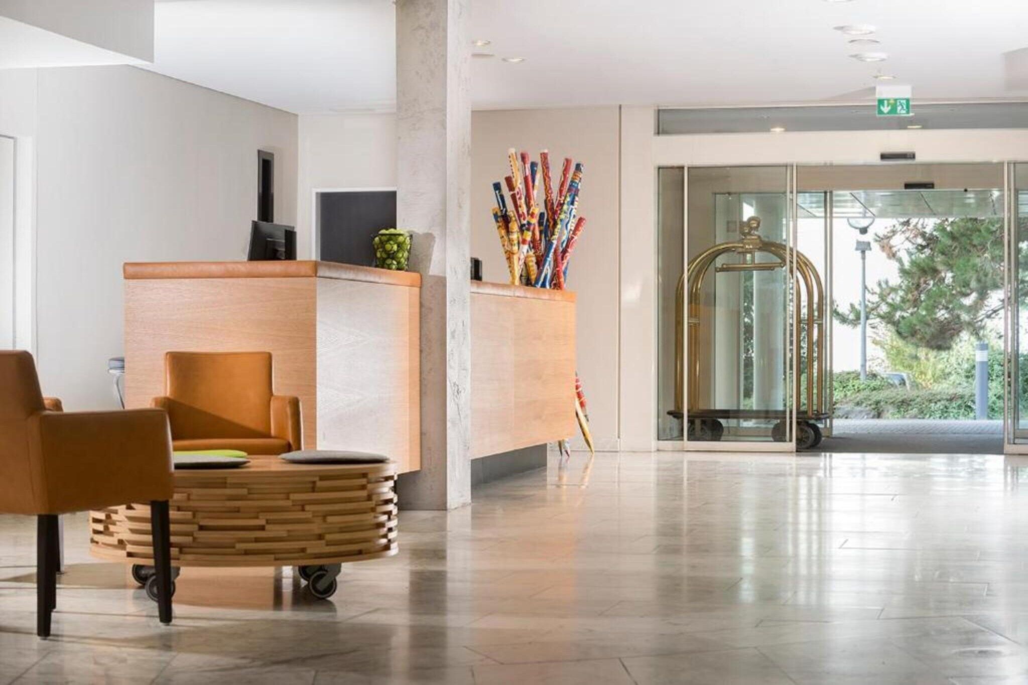 A modern reception area with a wooden reception desk, a seating area with a round table, and a glass door leading outside.
