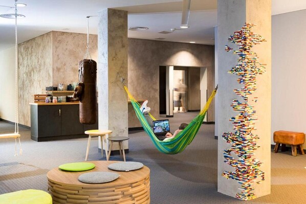 A modern lounge area with a hammock, a round wooden table, and a wall art installation.