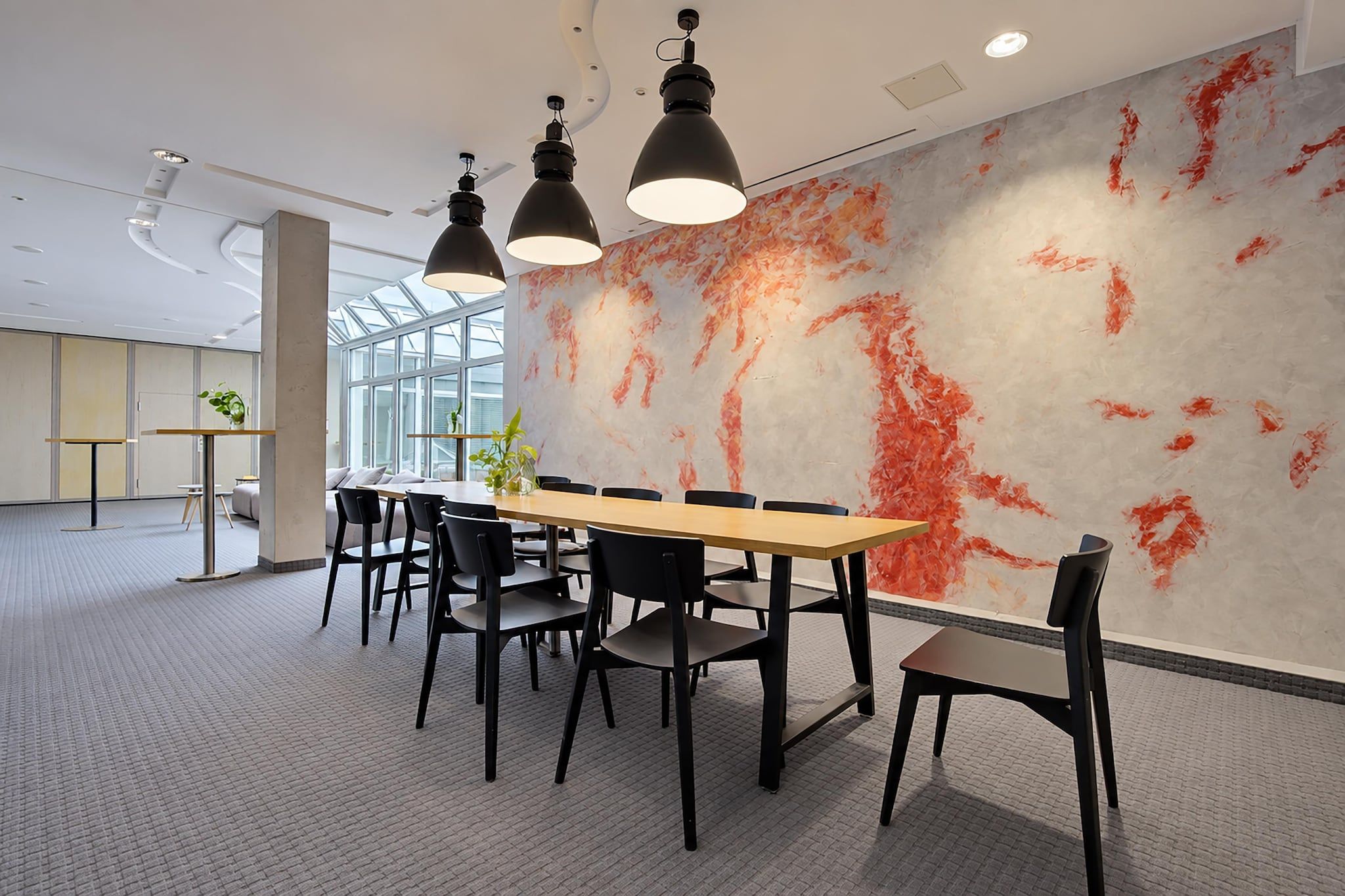 A modern conference room with a long table, black chairs, and pendant lighting.