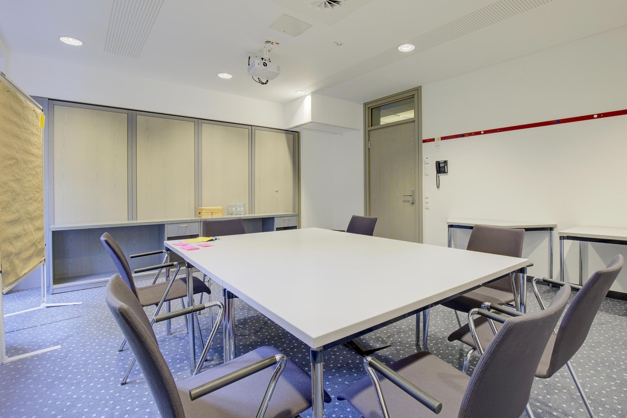 Une salle de conférence équipée d’une grande table, de chaises, d’un projecteur et d’un téléphone fixé au mur.