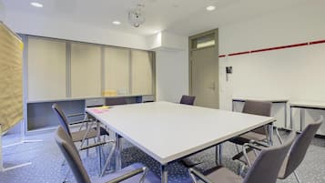 Une salle de conférence équipée d’une grande table, de chaises, d’un projecteur et d’un téléphone fixé au mur.