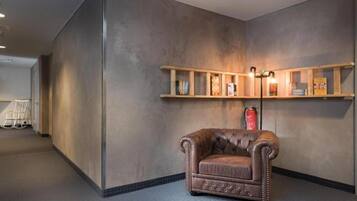 A room with a brown leather armchair, a wooden shelf with books, and a fire extinguisher on the wall.