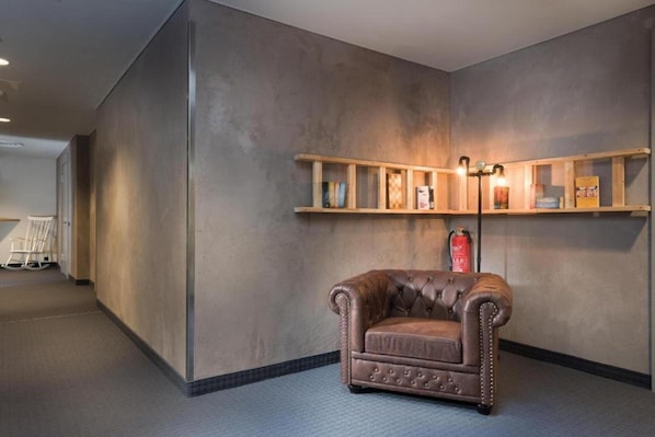 A room with a brown leather armchair, a wooden shelf with books, and a fire extinguisher on the wall.