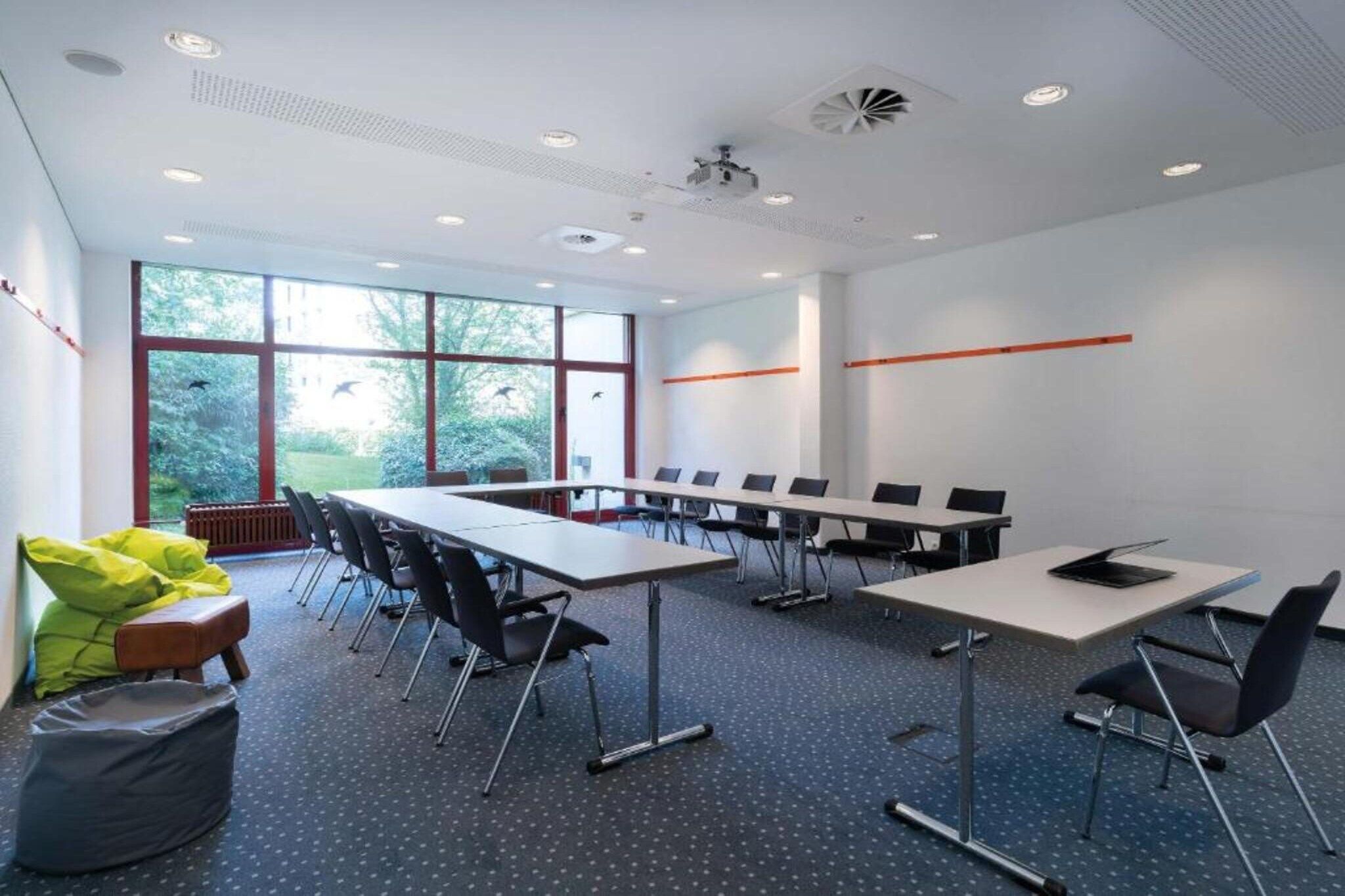 Konferenssihuone, jossa on pitkä pöytä, tuoleja ja projektori.