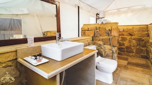 Et badeværelse med hvid vask, spejl, brusebad med stenvæg og toilet.