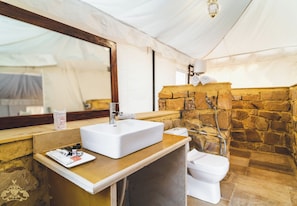 Une salle de bain avec un lavabo blanc, un miroir, une douche avec un mur en pierre et des toilettes.