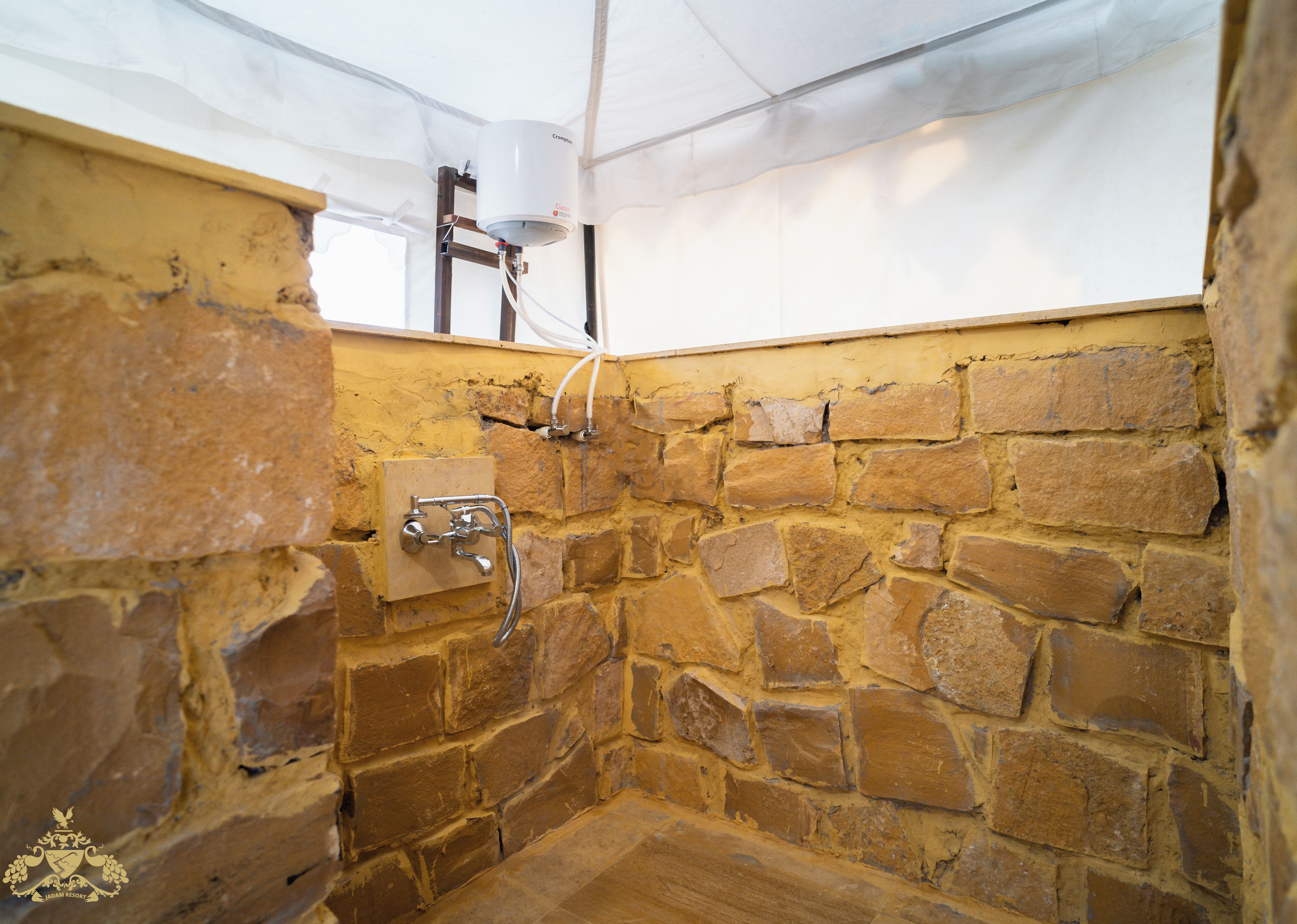 Un baño con paredes de piedra, una ducha, techo blanco y calentador de agua a la vista.