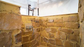 Un baño con paredes de piedra, una ducha, techo blanco y calentador de agua a la vista.