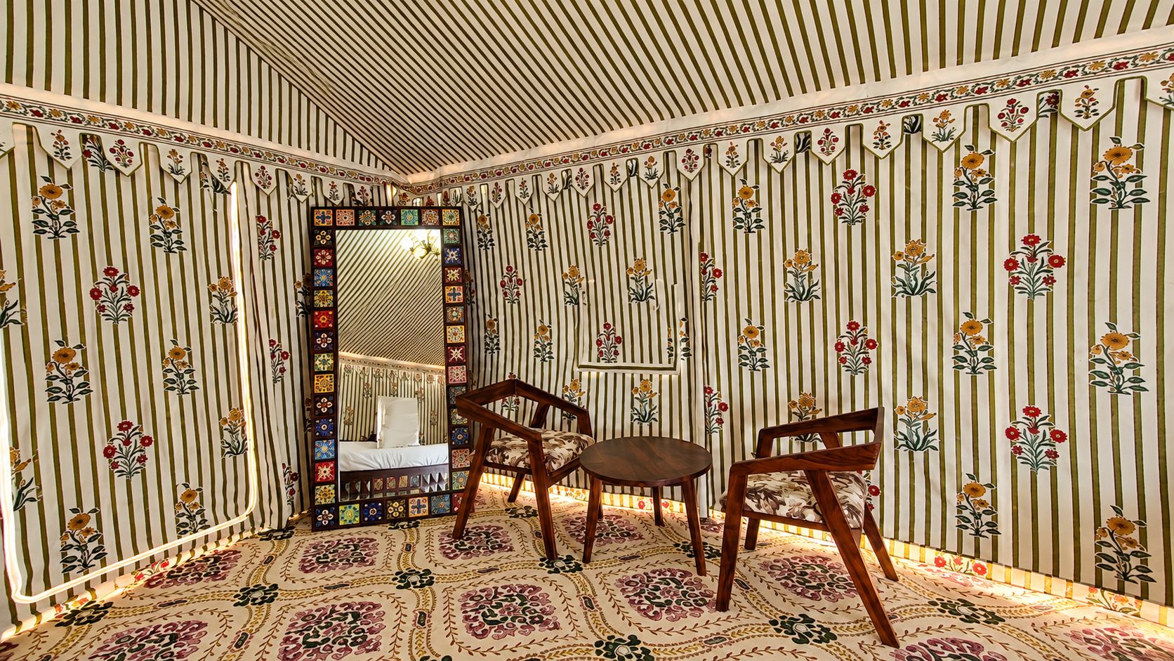 Quarto com papel de parede listrado, uma cama, uma cadeira, uma mesa e um espelho.