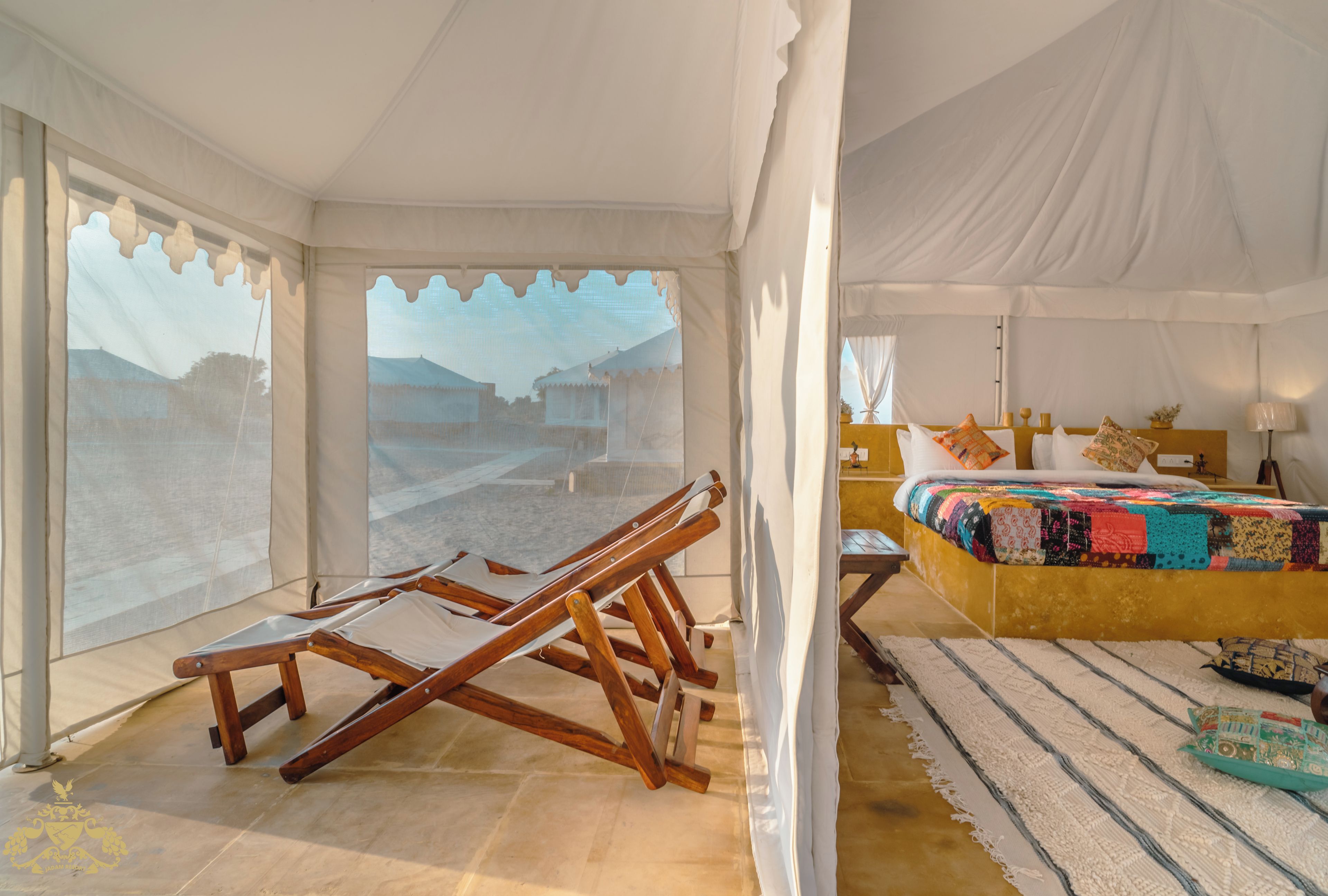 A tented room with a bed, a wooden chair, and a view of a mountainous landscape.