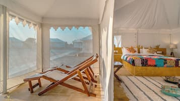 A tented room with a bed, a wooden chair, and a view of a mountainous landscape.
