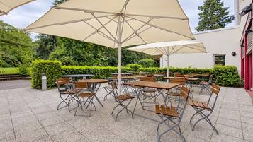 Une terrasse extérieure avec des tables et des chaises rondes, de grands parasols et un sol carrelé.